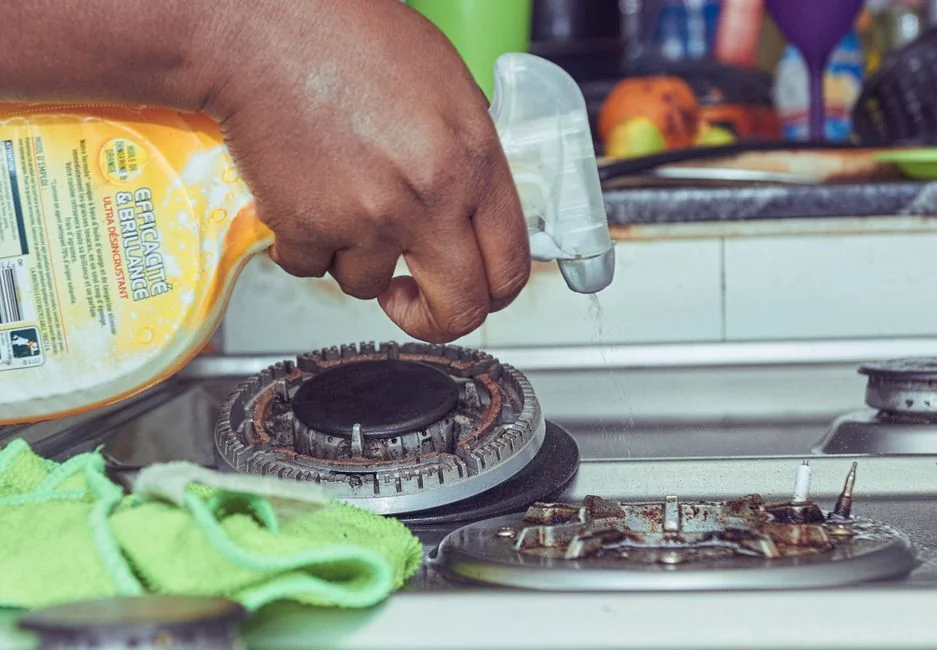 Person in protective gear sanitizing kitchen surfaces with disinfectant.